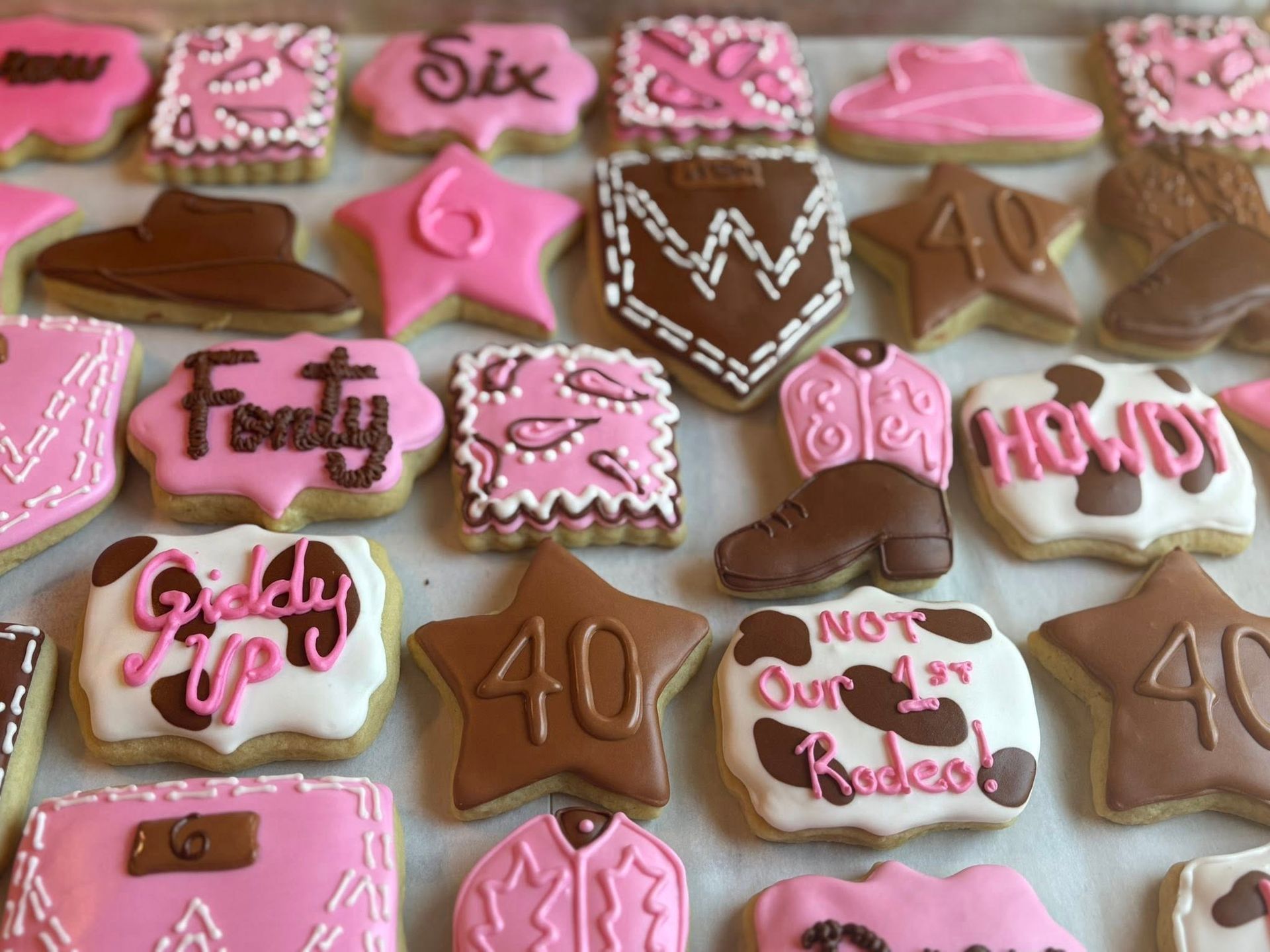 Assortment of decorated sugar cookies in pink and brown with western and birthday themes. Base Camp Bakery Gunnison, Colorado https://share.google/AgqUzUKNzsb0ThlP5, https://www.facebook.com/BaseCampBakery1, https://www.instagram.com/basecampbakery_81230