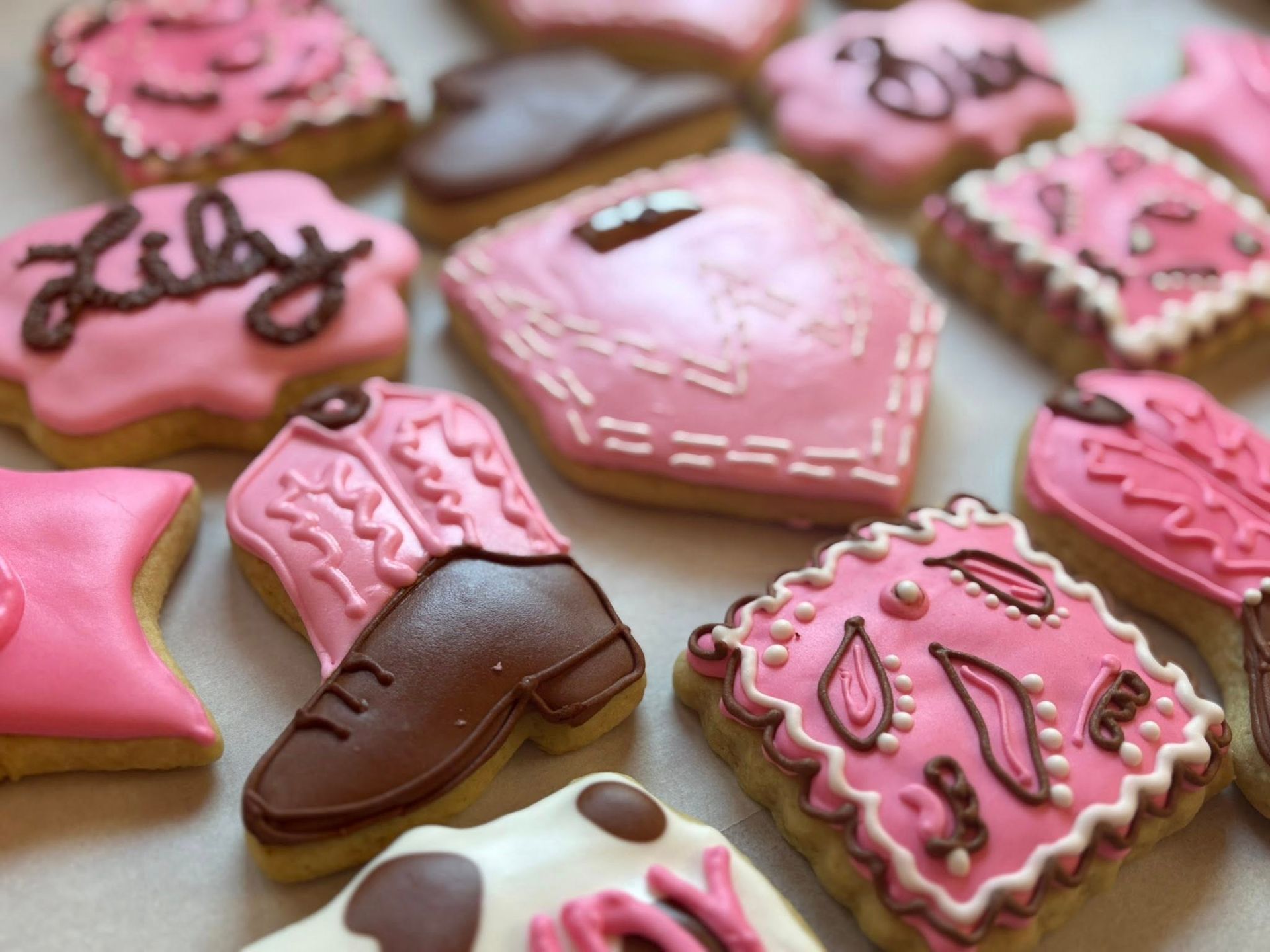 Pink frosted decorated cookies, including cowboy boot, with names, and floral and geometric designs. Base Camp Bakery Gunnison, Colorado https://share.google/AgqUzUKNzsb0ThlP5, https://www.facebook.com/BaseCampBakery1, https://www.instagram.com/basecampbakery_81230