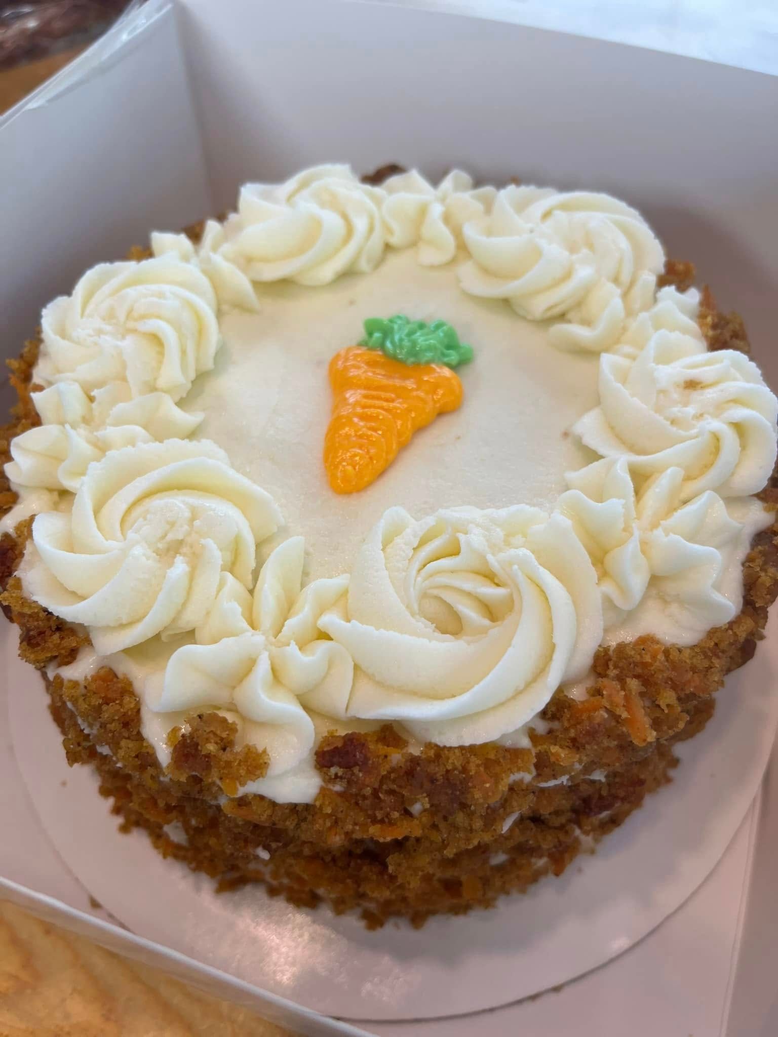 Carrot cake with white frosting swirls and a candy carrot on top. Base Camp Bakery Gunnison, Colorado https://share.google/AgqUzUKNzsb0ThlP5, https://www.facebook.com/BaseCampBakery1, https://www.instagram.com/basecampbakery_81230