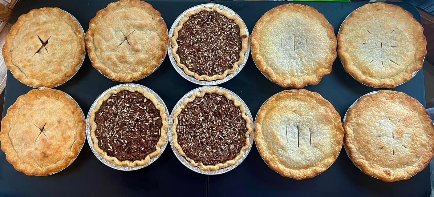 Ten baked pies of varying types are displayed on a dark surface. Base Camp Bakery Gunnison, Colorado https://share.google/AgqUzUKNzsb0ThlP5, https://www.facebook.com/BaseCampBakery1, https://www.instagram.com/basecampbakery_81230