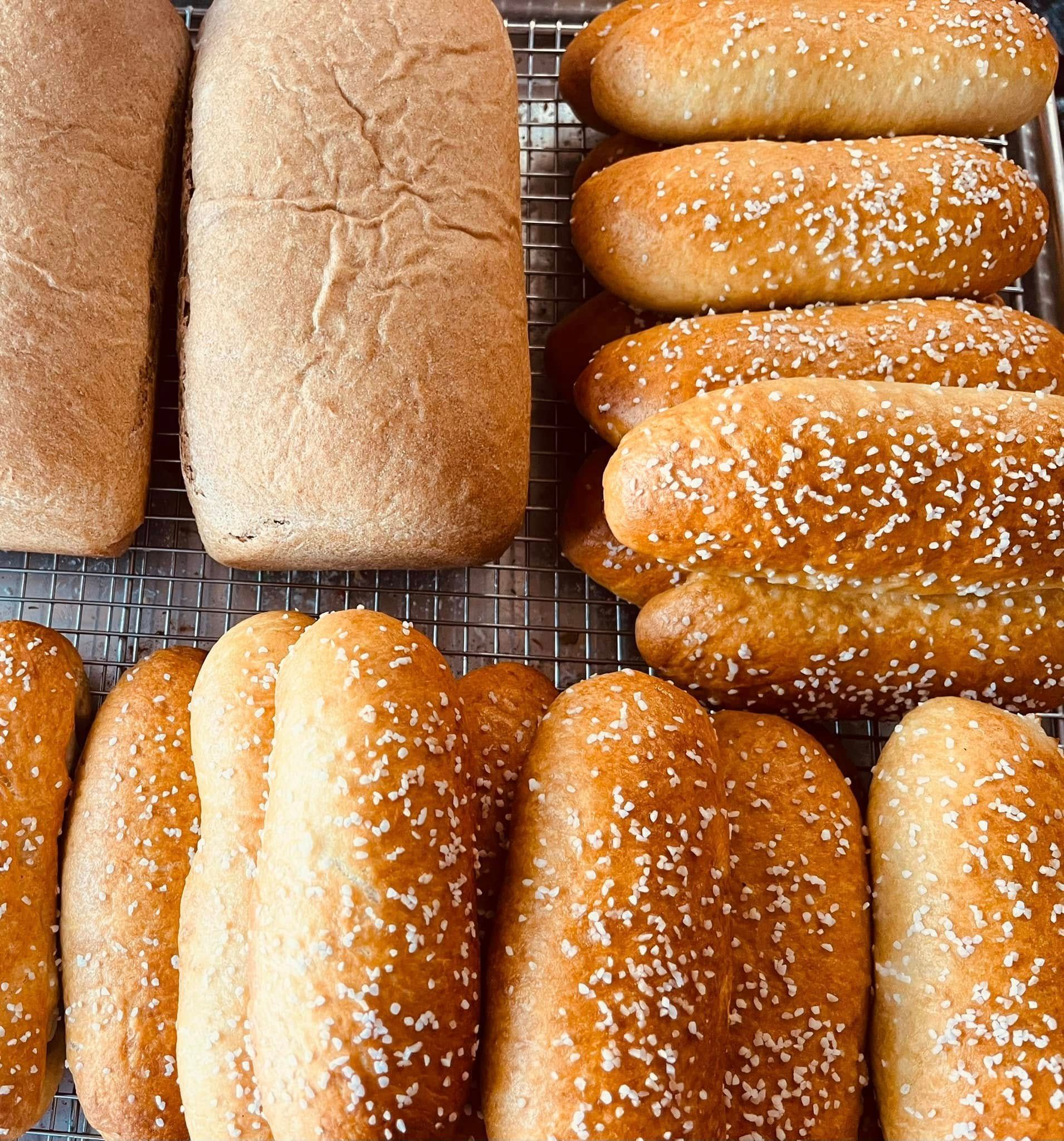 Freshly baked bread rolls and loaves on a wire rack, some with sesame seeds. Base Camp Bakery Gunnison, Colorado https://share.google/AgqUzUKNzsb0ThlP5, https://www.facebook.com/BaseCampBakery1, https://www.instagram.com/basecampbakery_81230