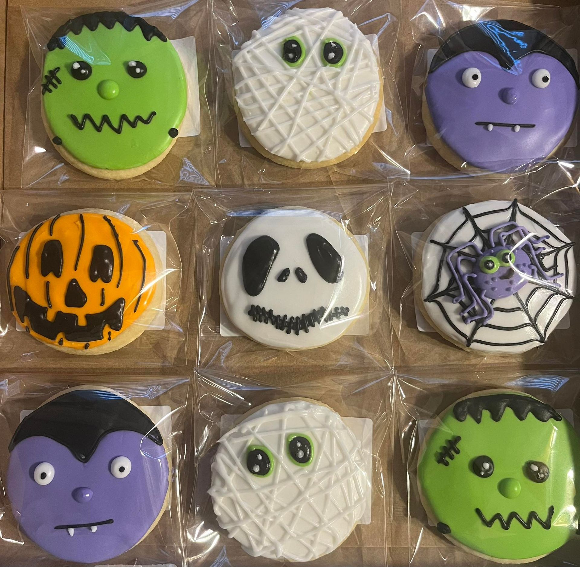 Nine Halloween-themed cookies in a box: Frankenstein, mummy, vampire, pumpkin, Jack Skellington, spiderweb, etc. Base Camp Bakery Gunnison, Colorado https://share.google/AgqUzUKNzsb0ThlP5, https://www.facebook.com/BaseCampBakery1, https://www.instagram.com/basecampbakery_81230