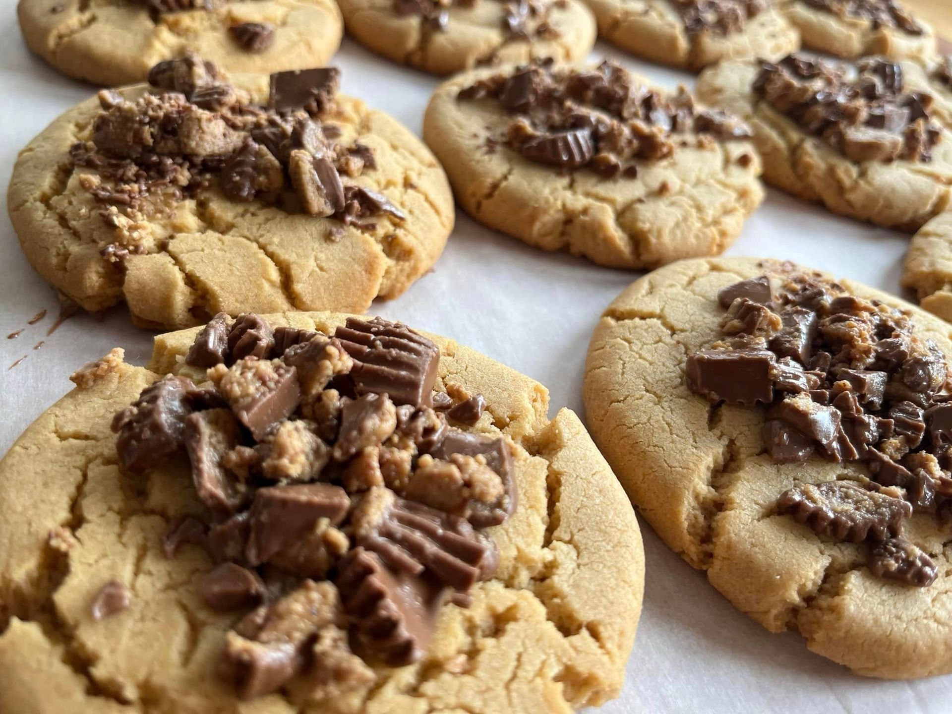 Peanut butter cookies topped with chopped peanut butter cups on parchment paper. Base Camp Bakery Gunnison, Colorado https://share.google/AgqUzUKNzsb0ThlP5, https://www.facebook.com/BaseCampBakery1, https://www.instagram.com/basecampbakery_81230