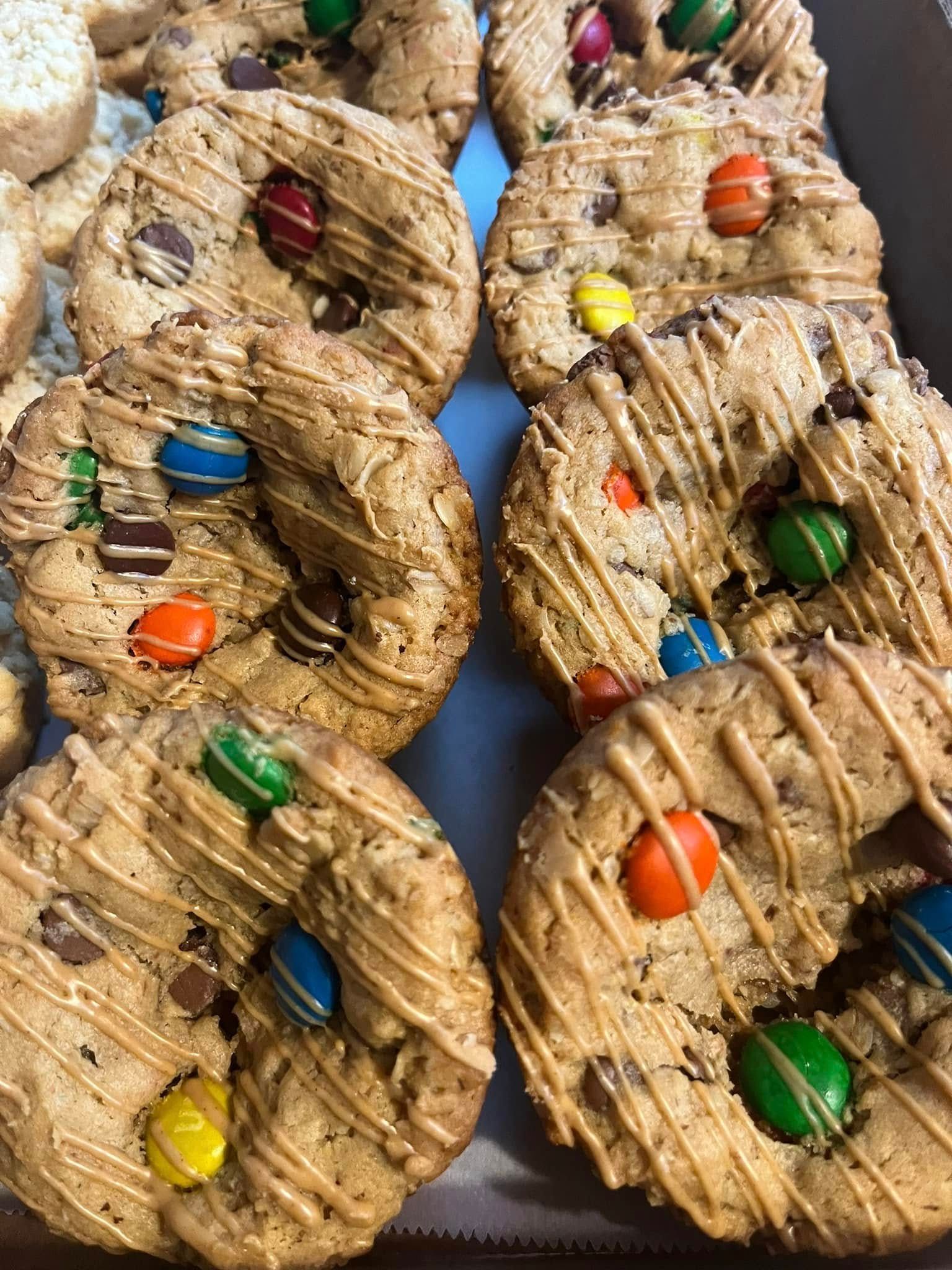 Close-up of a tray of round, decorated cookies with chocolate chips and candies, drizzled with caramel. Base Camp Bakery Gunnison, Colorado https://share.google/AgqUzUKNzsb0ThlP5, https://www.facebook.com/BaseCampBakery1, https://www.instagram.com/basecampbakery_81230