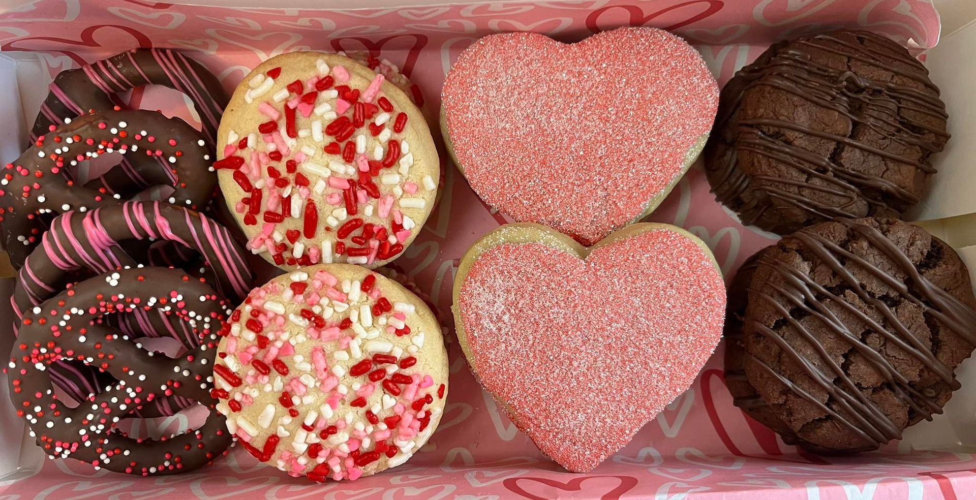Valentine's Day cookie box: chocolate-covered pretzels, frosted circles with sprinkles, and pink heart cookies. Base Camp Bakery Gunnison, Colorado https://share.google/AgqUzUKNzsb0ThlP5, https://www.facebook.com/BaseCampBakery1, https://www.instagram.com/basecampbakery_81230