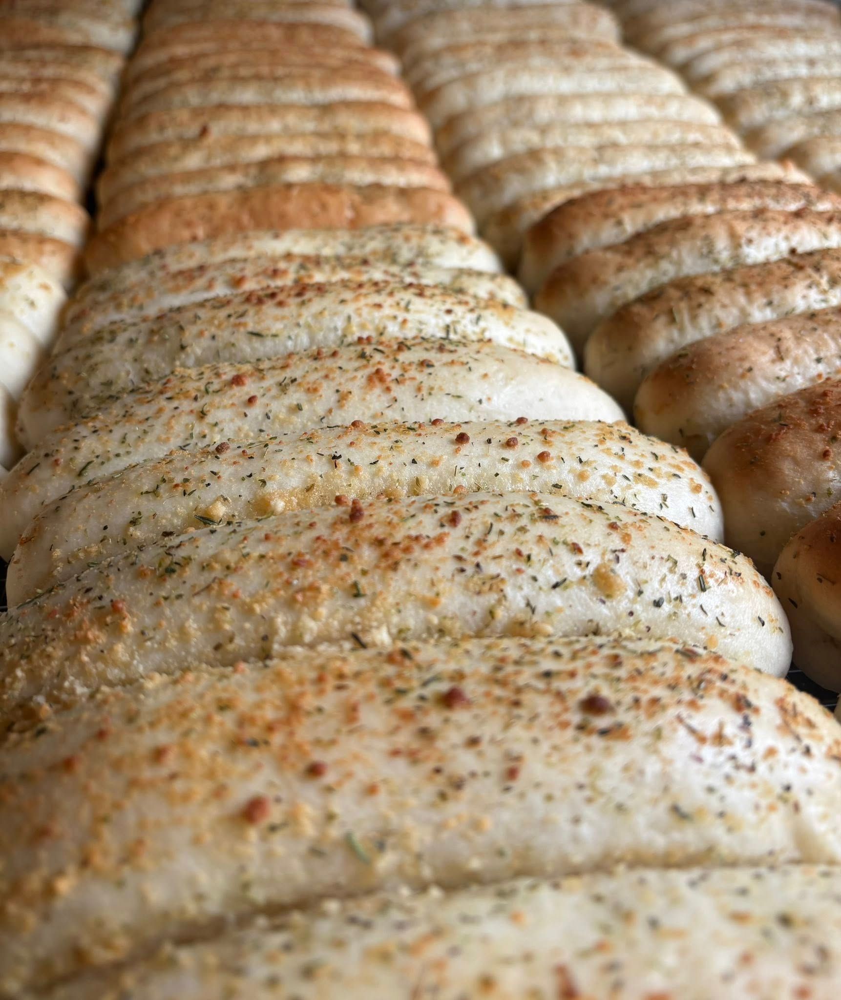 Rows of freshly baked breadsticks, seasoned with herbs and spices. Base Camp Bakery Gunnison, Colorado https://share.google/AgqUzUKNzsb0ThlP5, https://www.facebook.com/BaseCampBakery1, https://www.instagram.com/basecampbakery_81230