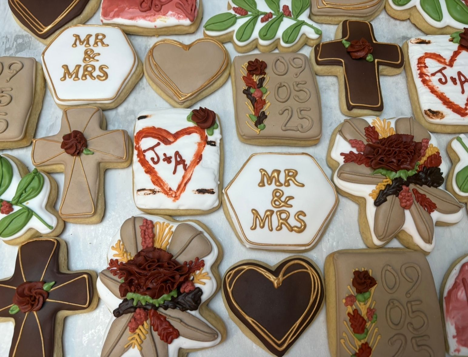 Wedding cookies decorated with white, brown, and gold frosting, with hearts, crosses. Base Camp Bakery Gunnison, Colorado https://share.google/AgqUzUKNzsb0ThlP5, https://www.facebook.com/BaseCampBakery1, https://www.instagram.com/basecampbakery_81230