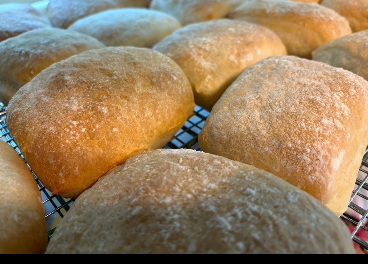 Golden-brown rolls dusted with flour on a wire rack. Base Camp Bakery Gunnison, Colorado https://share.google/AgqUzUKNzsb0ThlP5, https://www.facebook.com/BaseCampBakery1, https://www.instagram.com/basecampbakery_81230