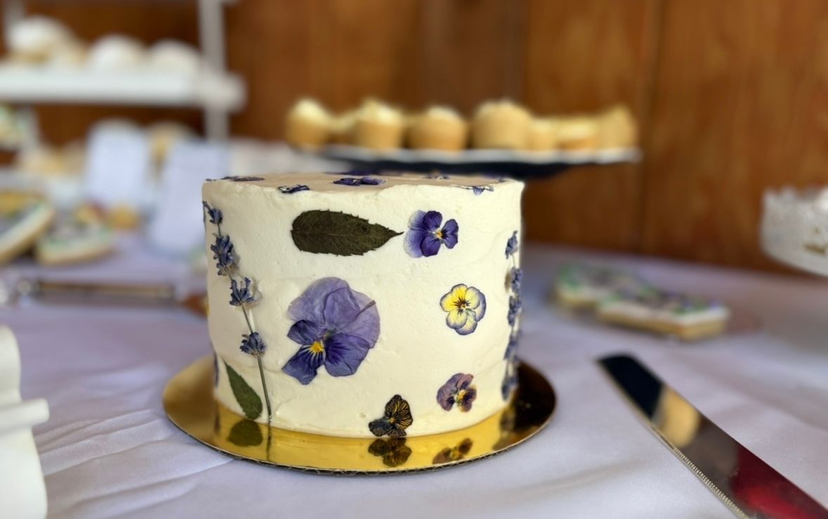Cake with edible pressed flowers. White frosting with purple, yellow, and green floral decorations.