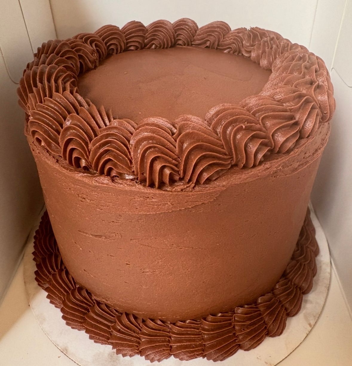 Chocolate cake with smooth frosting and decorative piped border. Base Camp Bakery Gunnison, Colorado https://share.google/AgqUzUKNzsb0ThlP5, https://www.facebook.com/BaseCampBakery1, https://www.instagram.com/basecampbakery_81230