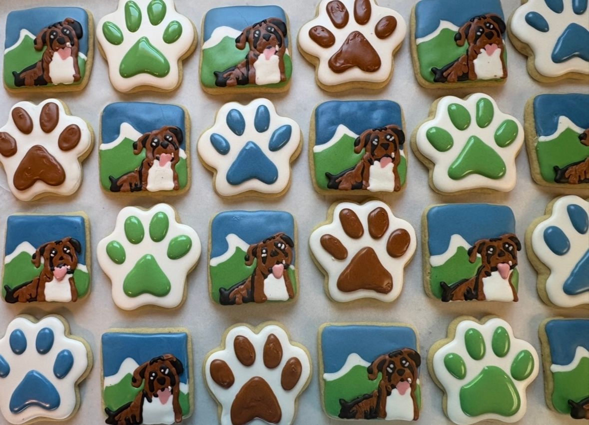 Cookies decorated with paw prints and a dog against a mountain backdrop. Various colors: brown, blue, and green. Base Camp Bakery Gunnison, Colorado https://share.google/AgqUzUKNzsb0ThlP5, https://www.facebook.com/BaseCampBakery1, https://www.instagram.com/basecampbakery_81230
