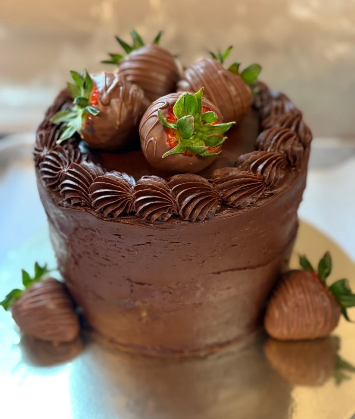 Chocolate cake with chocolate-covered strawberries on a silver surface.