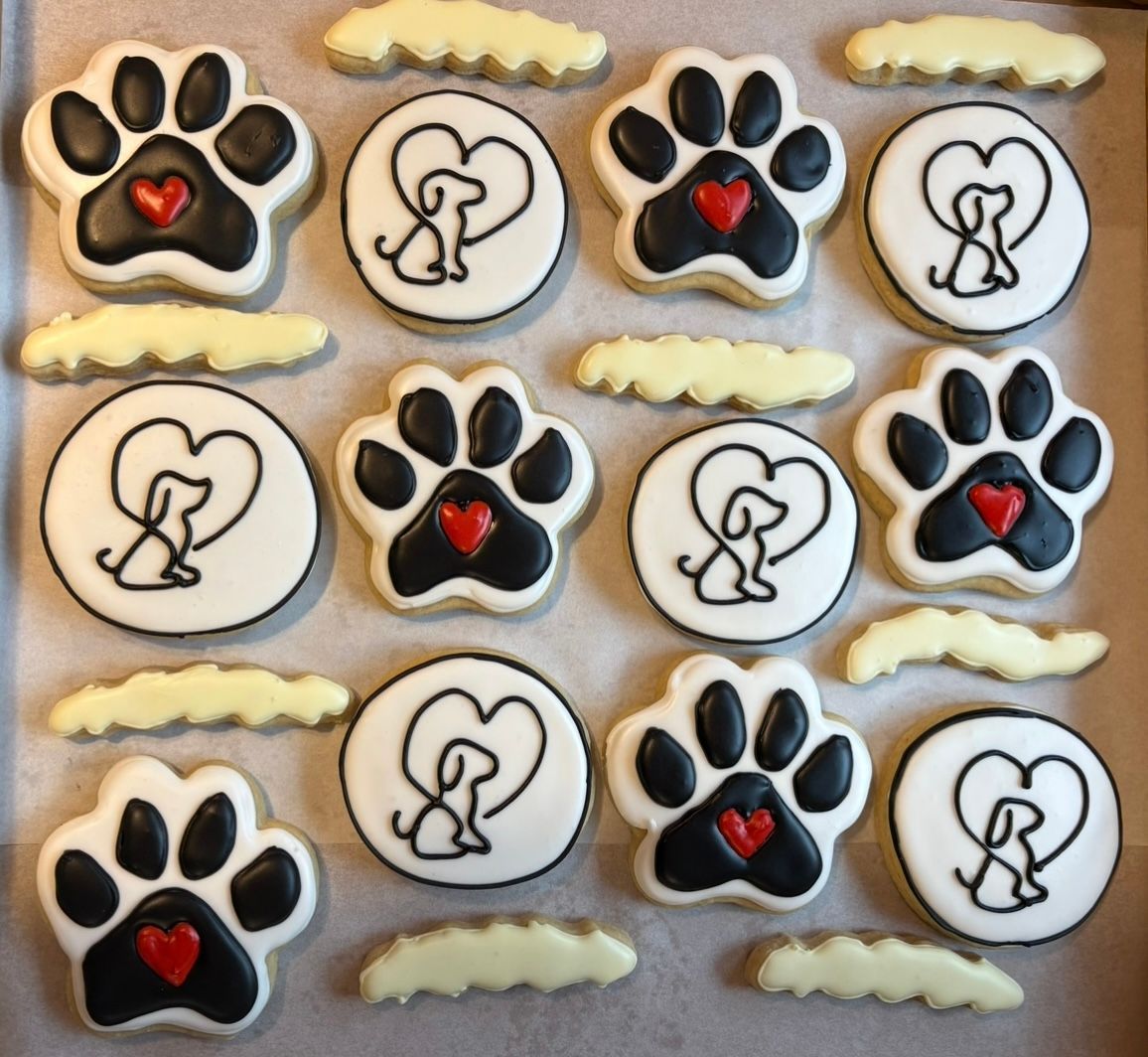 Tray of decorated dog-themed cookies: paw prints with hearts, dogs in hearts, and cloud shapes. Base Camp Bakery Gunnison, Colorado https://share.google/AgqUzUKNzsb0ThlP5, https://www.facebook.com/BaseCampBakery1, https://www.instagram.com/basecampbakery_81230