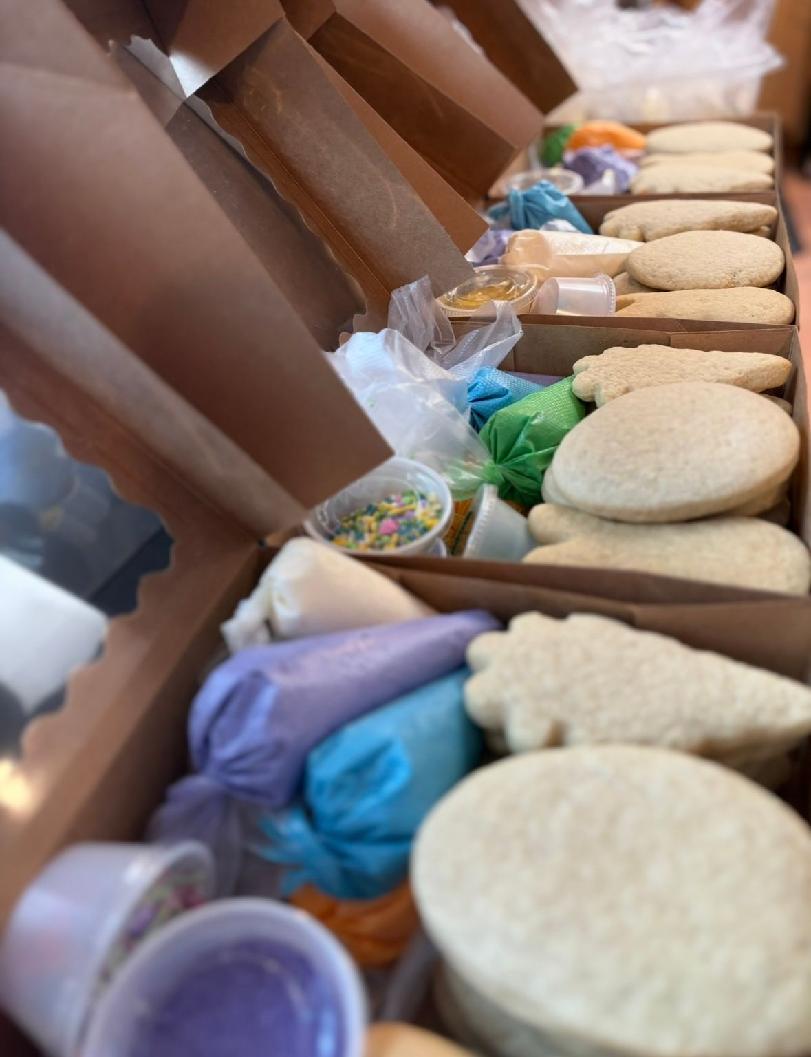 Cookie decorating kits in open cardboard boxes, with cookies, icing bags, and sprinkles visible.