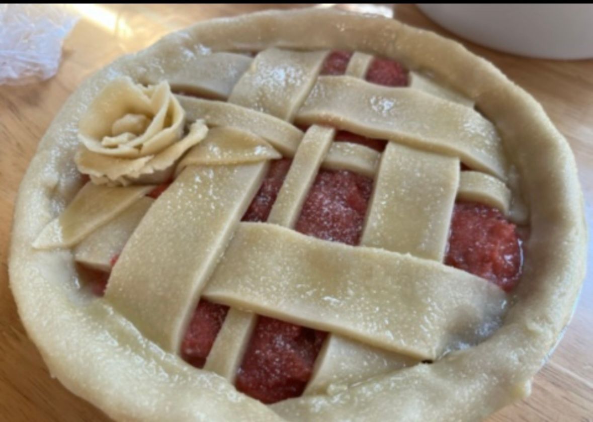 Mini pie with lattice crust and dough rose, filled with red filling, on wooden surface. Base Camp Bakery Gunnison, Colorado https://share.google/AgqUzUKNzsb0ThlP5, https://www.facebook.com/BaseCampBakery1, https://www.instagram.com/basecampbakery_81230