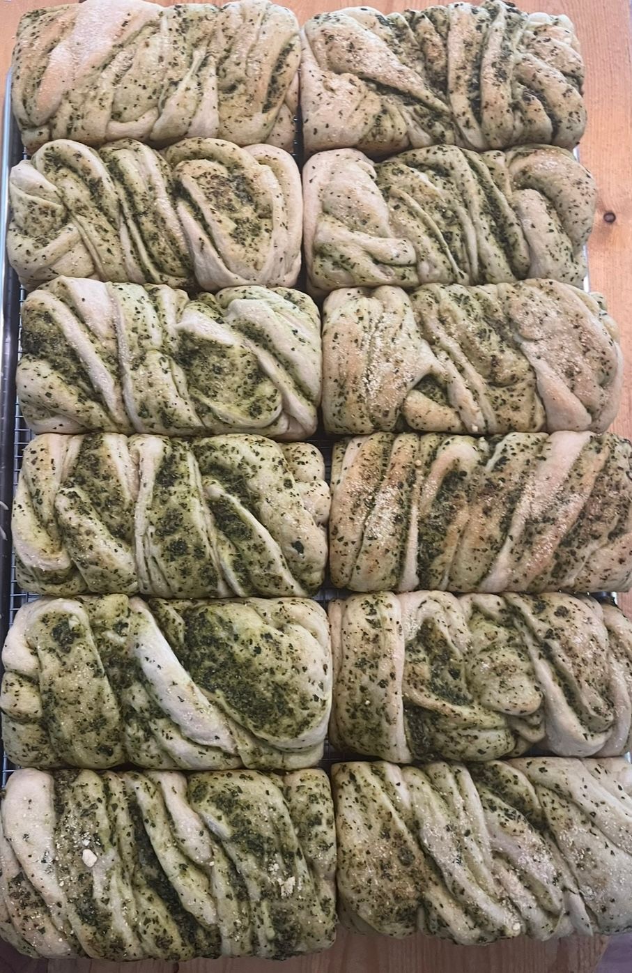 Rows of twisted bread, light and dark green marbled, on a wire rack. Base Camp Bakery Gunnison, Colorado https://share.google/AgqUzUKNzsb0ThlP5, https://www.facebook.com/BaseCampBakery1, https://www.instagram.com/basecampbakery_81230