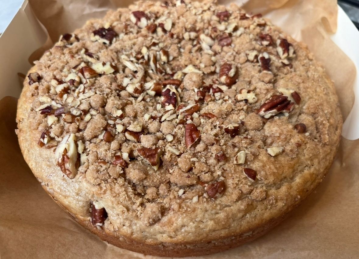 Coffee cake with pecan topping in a paper-lined container. Base Camp Bakery Gunnison, Colorado https://share.google/AgqUzUKNzsb0ThlP5, https://www.facebook.com/BaseCampBakery1, https://www.instagram.com/basecampbakery_81230