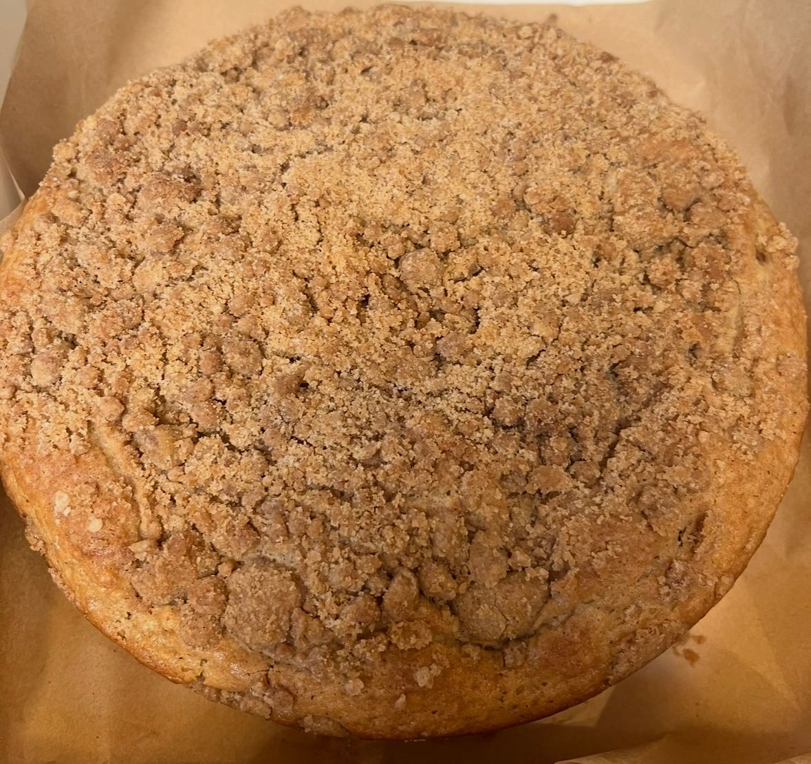 Round coffee cake with a crumb topping on parchment paper. Base Camp Bakery Gunnison, Colorado https://share.google/AgqUzUKNzsb0ThlP5, https://www.facebook.com/BaseCampBakery1, https://www.instagram.com/basecampbakery_81230