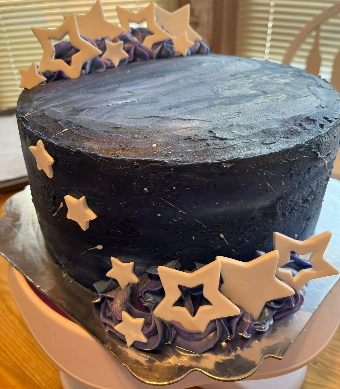 Cake decorated with navy blue frosting, white stars, and purple rosettes. Base Camp Bakery Gunnison, Colorado https://share.google/AgqUzUKNzsb0ThlP5, https://www.facebook.com/BaseCampBakery1, https://www.instagram.com/basecampbakery_81230