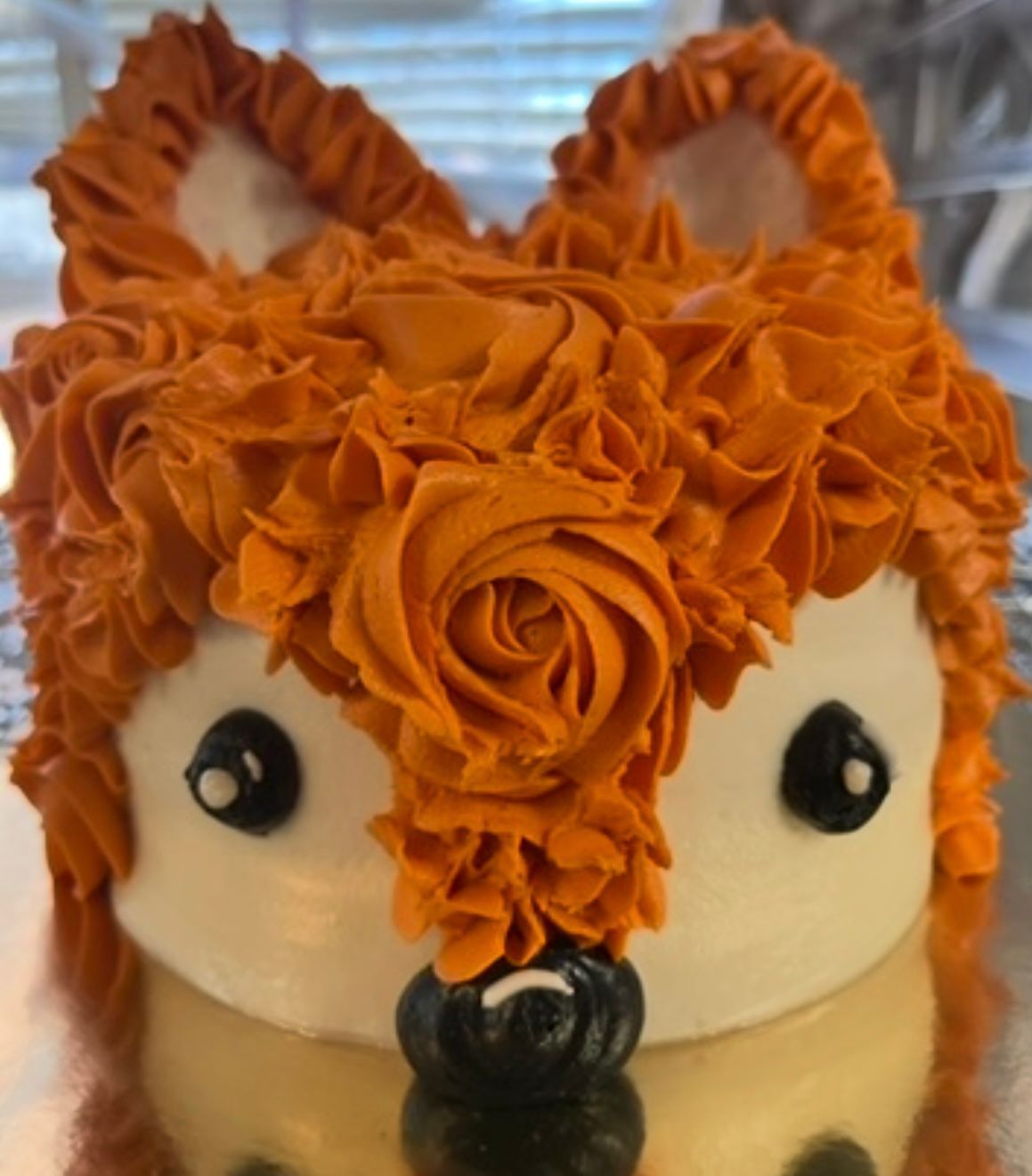 Fox-shaped cake decorated with orange frosting fur, white face, black eyes, and nose. Base Camp Bakery Gunnison, Colorado https://share.google/AgqUzUKNzsb0ThlP5, https://www.facebook.com/BaseCampBakery1, https://www.instagram.com/basecampbakery_81230