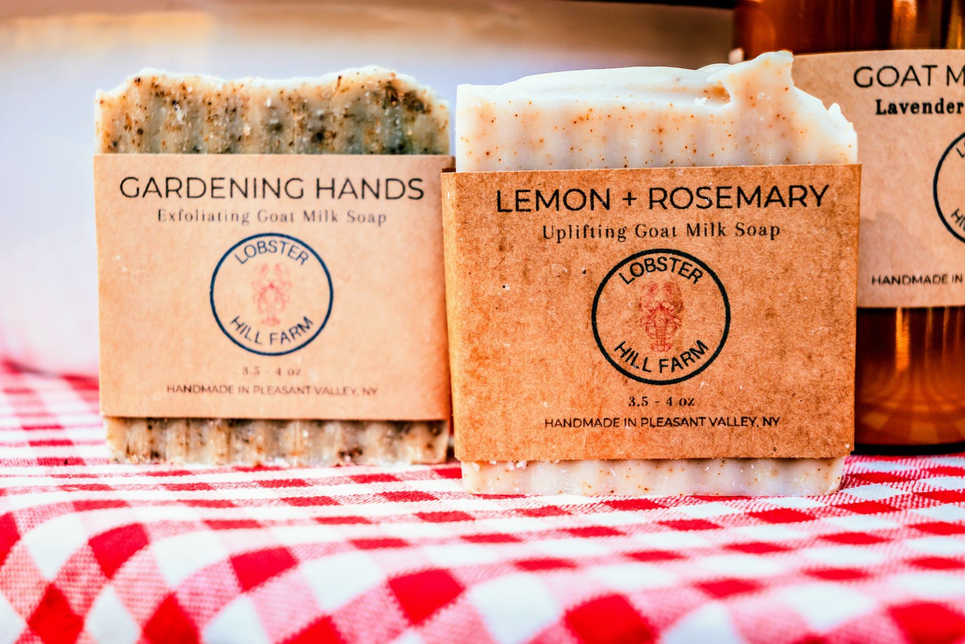 Two goat milk soaps with labels on a red-and-white checkered cloth.