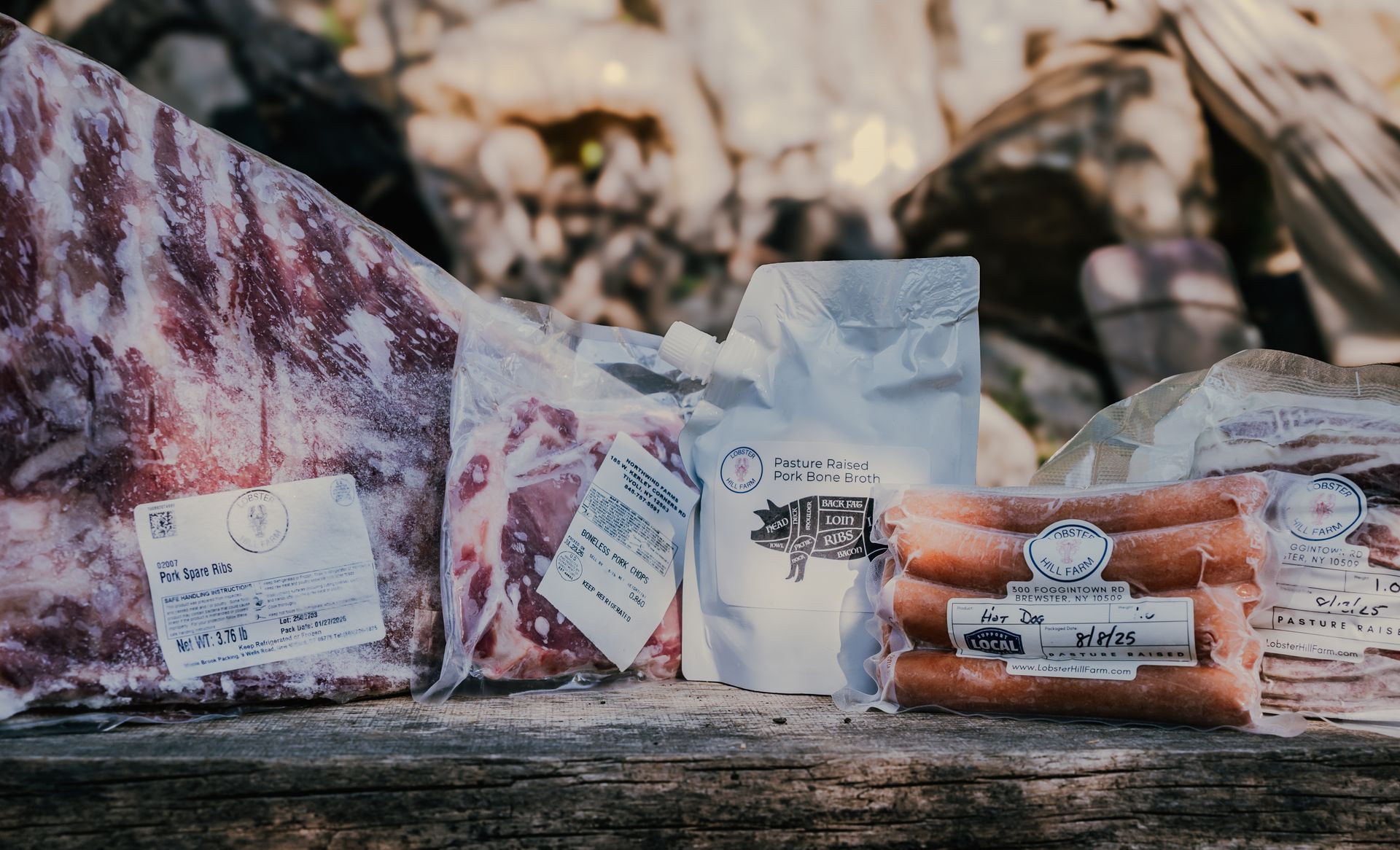 Frozen meat packages on a weathered wooden surface, including ribs and sausages, outdoor setting.
