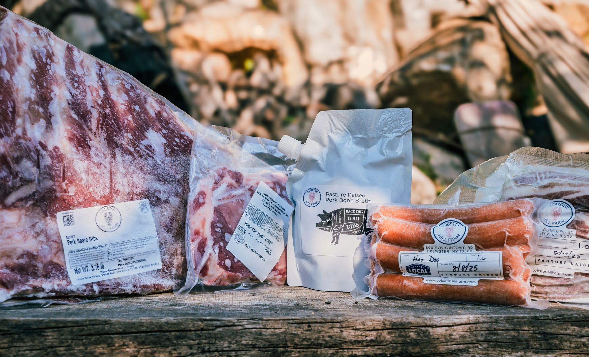 Assorted cuts of packaged raw meat on a rustic wooden surface outdoors.
