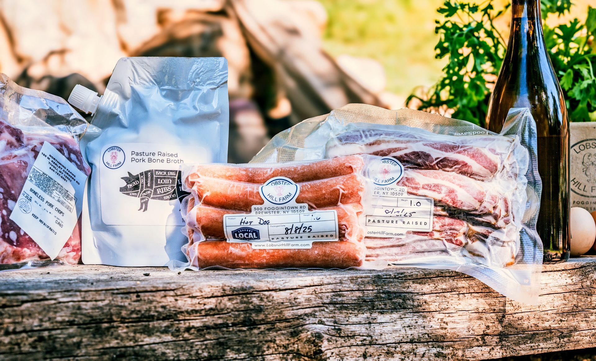 Various packaged meats and a bottle of dark liquid on a wooden surface, outdoor setting.