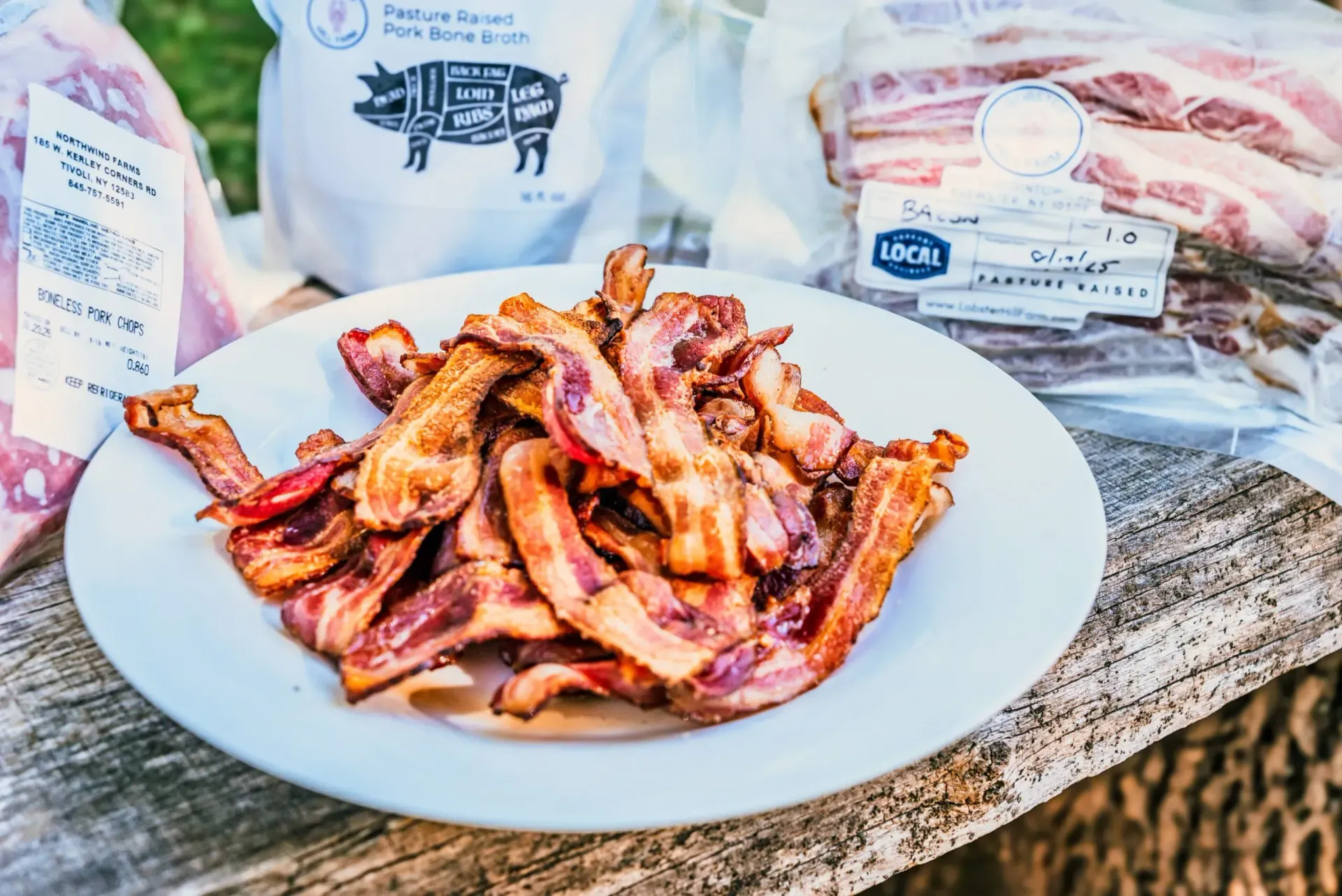 Plate of cooked bacon with packages of raw bacon and pork products in the background.