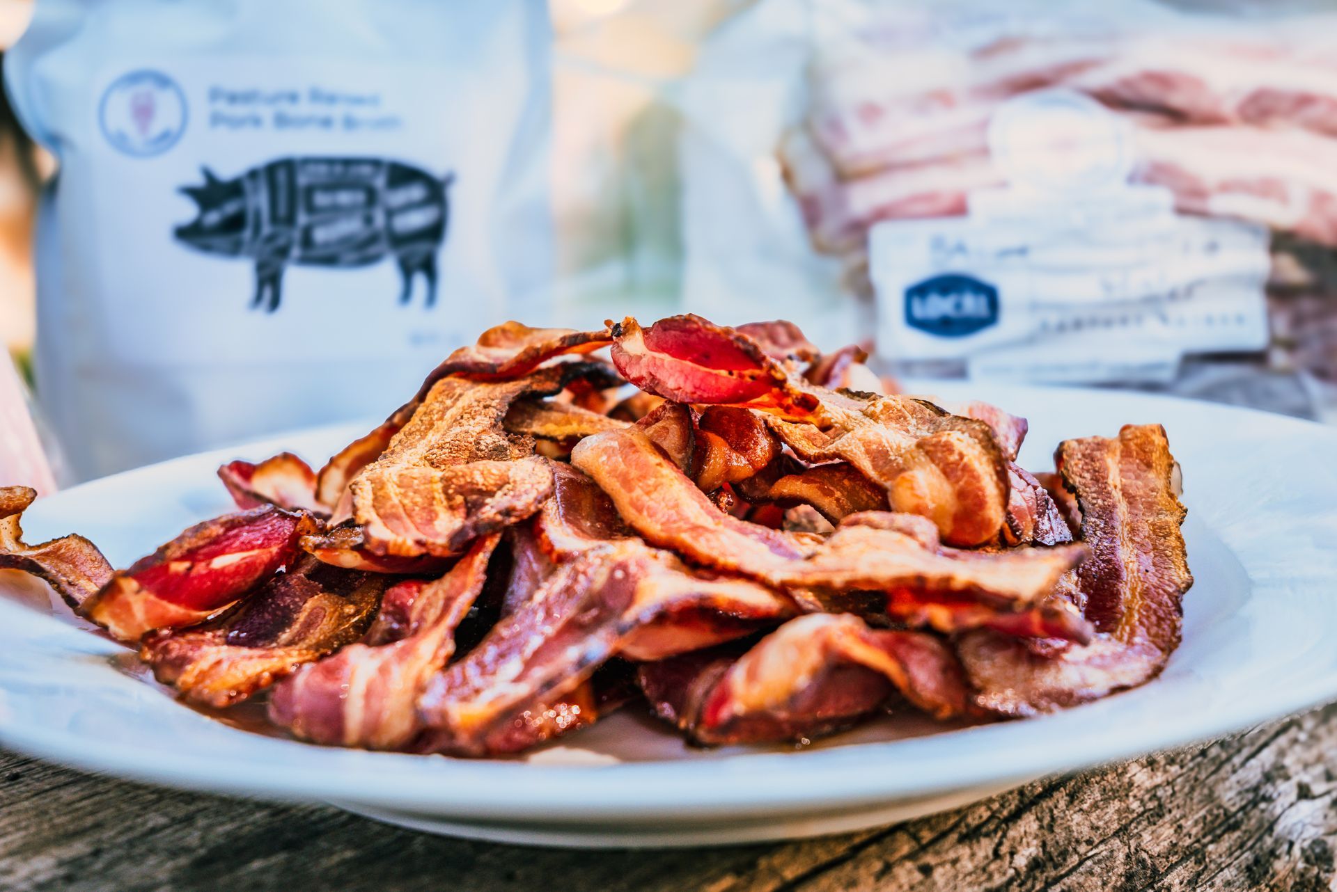 Plate of crispy bacon with bags of raw bacon in the background.