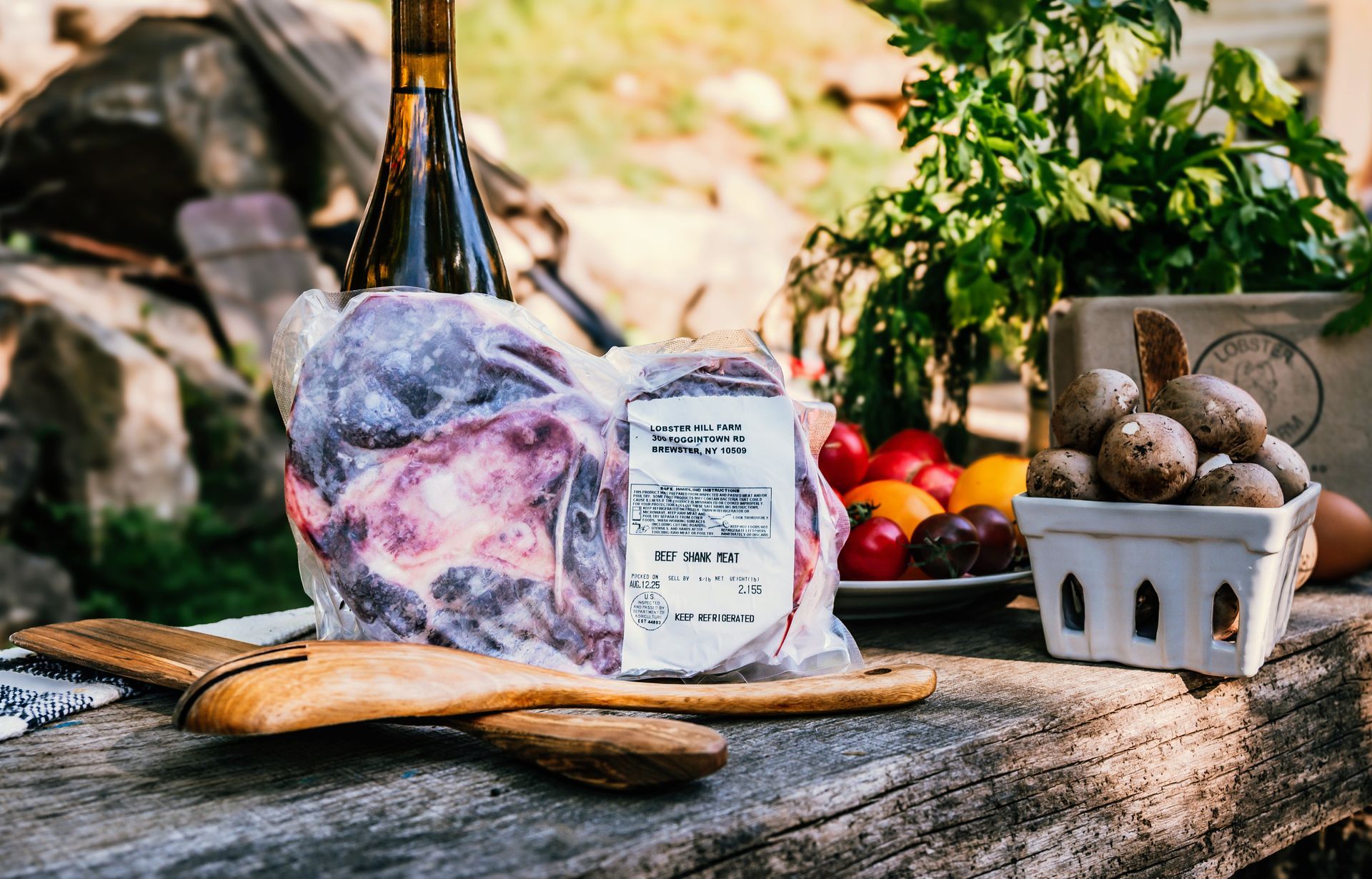 Meat in packaging with produce, wine, and wooden spoon on a rustic table.