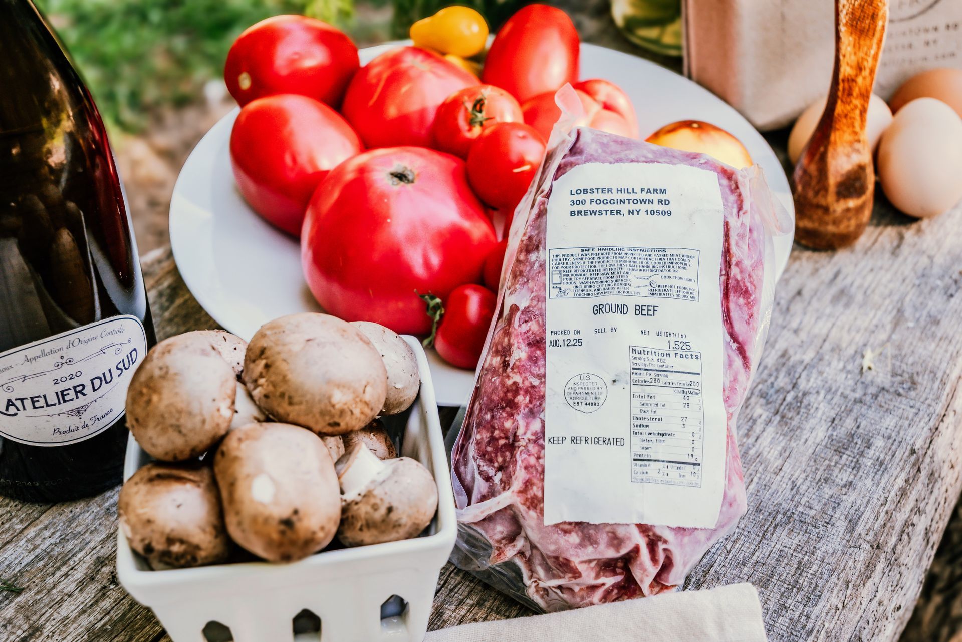 Tomatoes, mushrooms, ground meat, and eggs on a rustic wooden surface, with a bottle of wine.