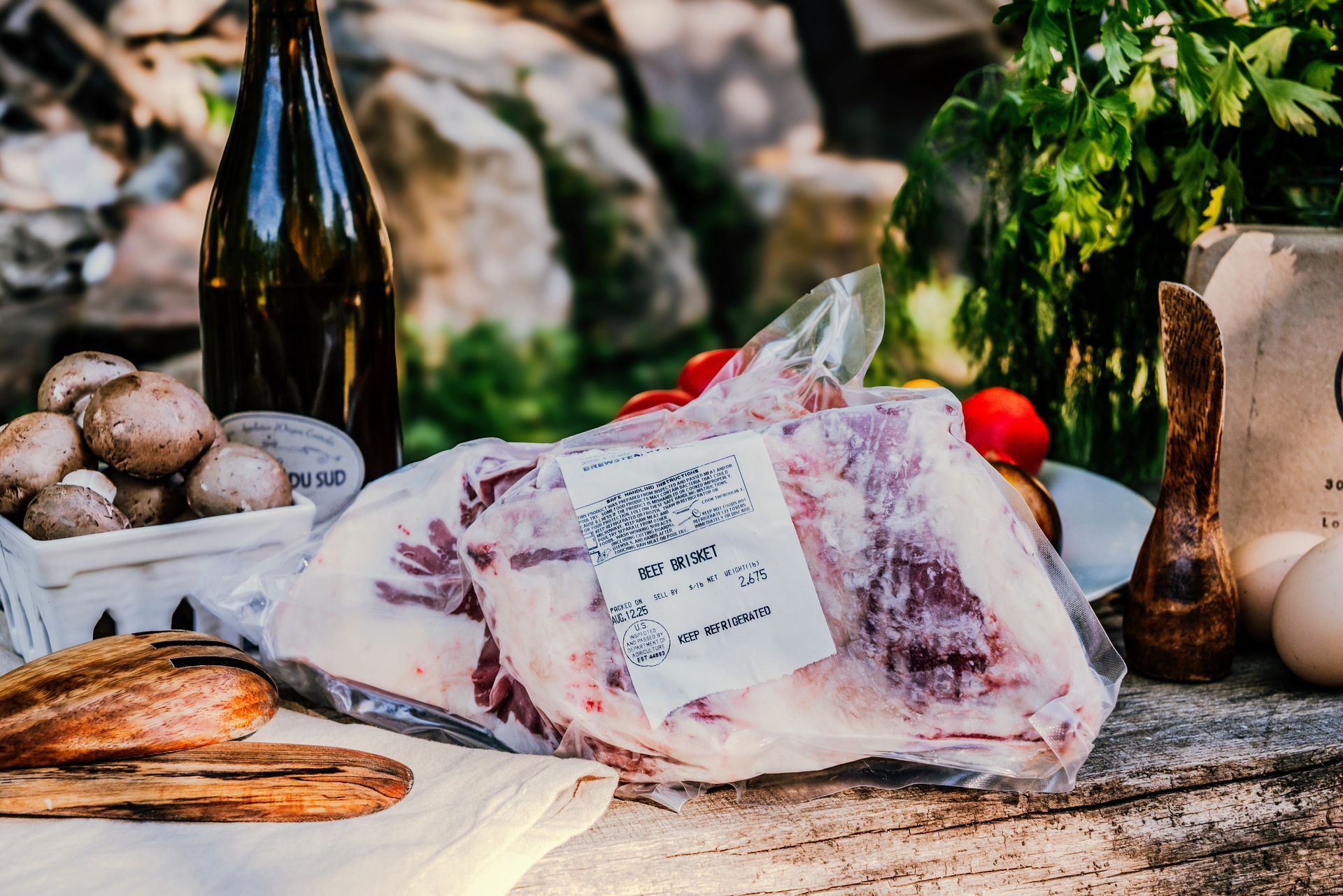 Raw packaged meat on a table with vegetables, bottle, eggs, and wooden tools.