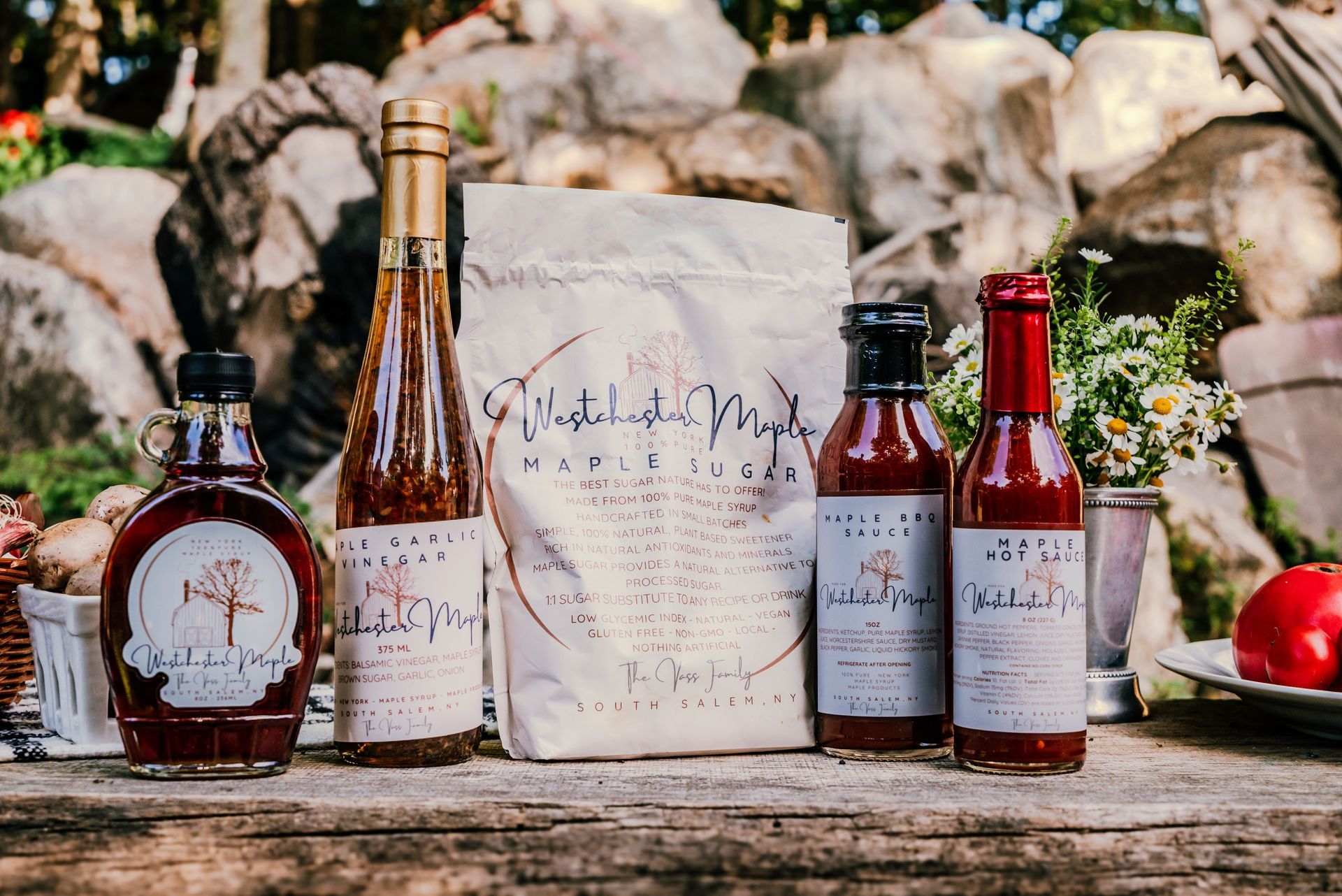 Assorted maple syrup products displayed on a wooden surface with a rocky background.
