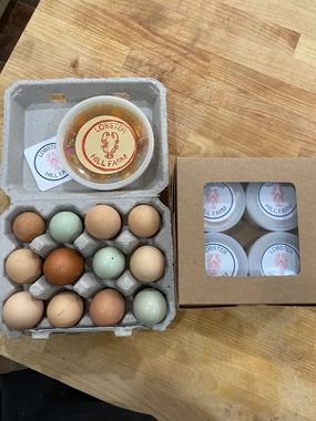 Carton of colorful eggs, a container of food with a label, and a box of small containers on a wooden surface.