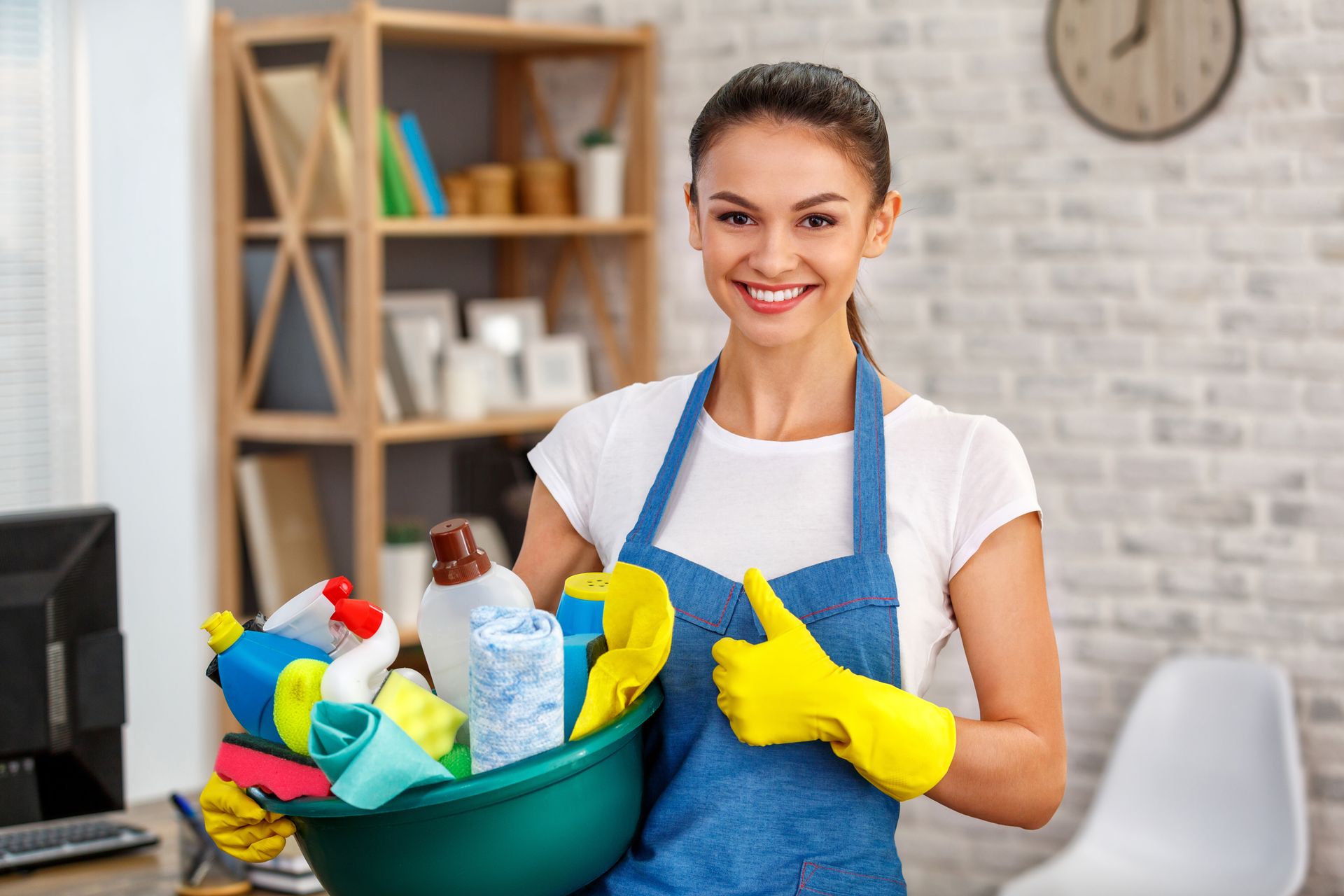 A woman is holding a bowl of cleaning supplies and giving a thumbs up.