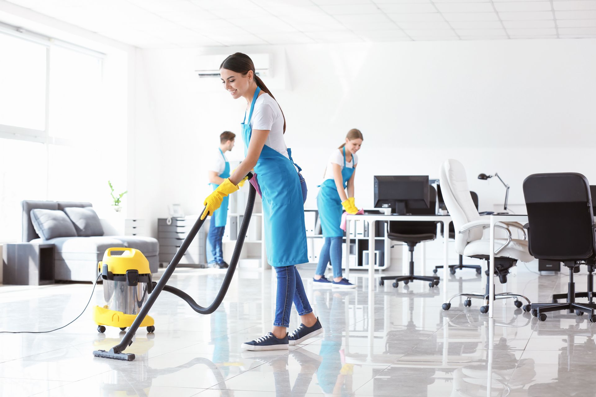 A woman is cleaning the floor of an office with a vacuum cleaner.
