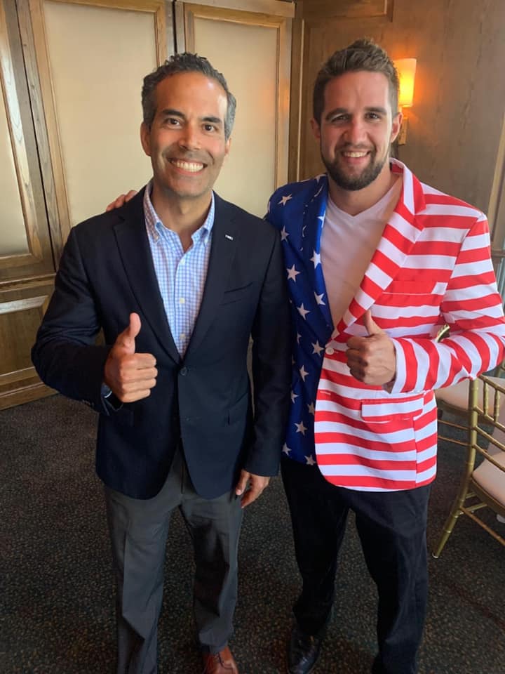 Two men are posing for a picture and one of them is wearing an american flag jacket.