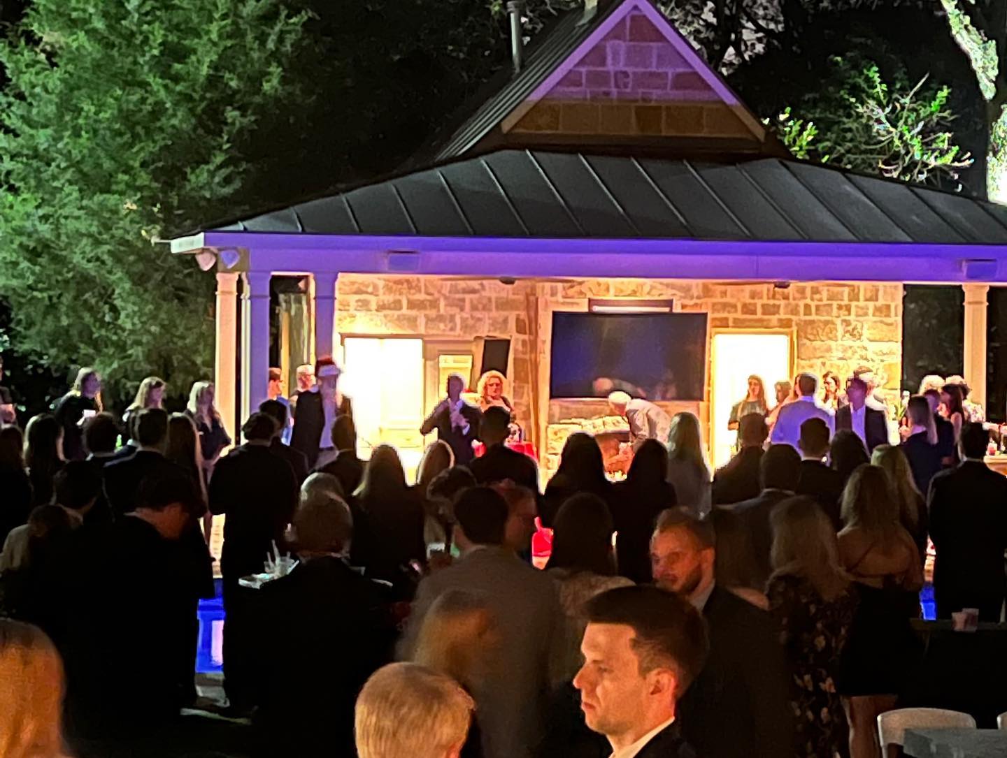 A large group of people are standing in front of a gazebo at night.