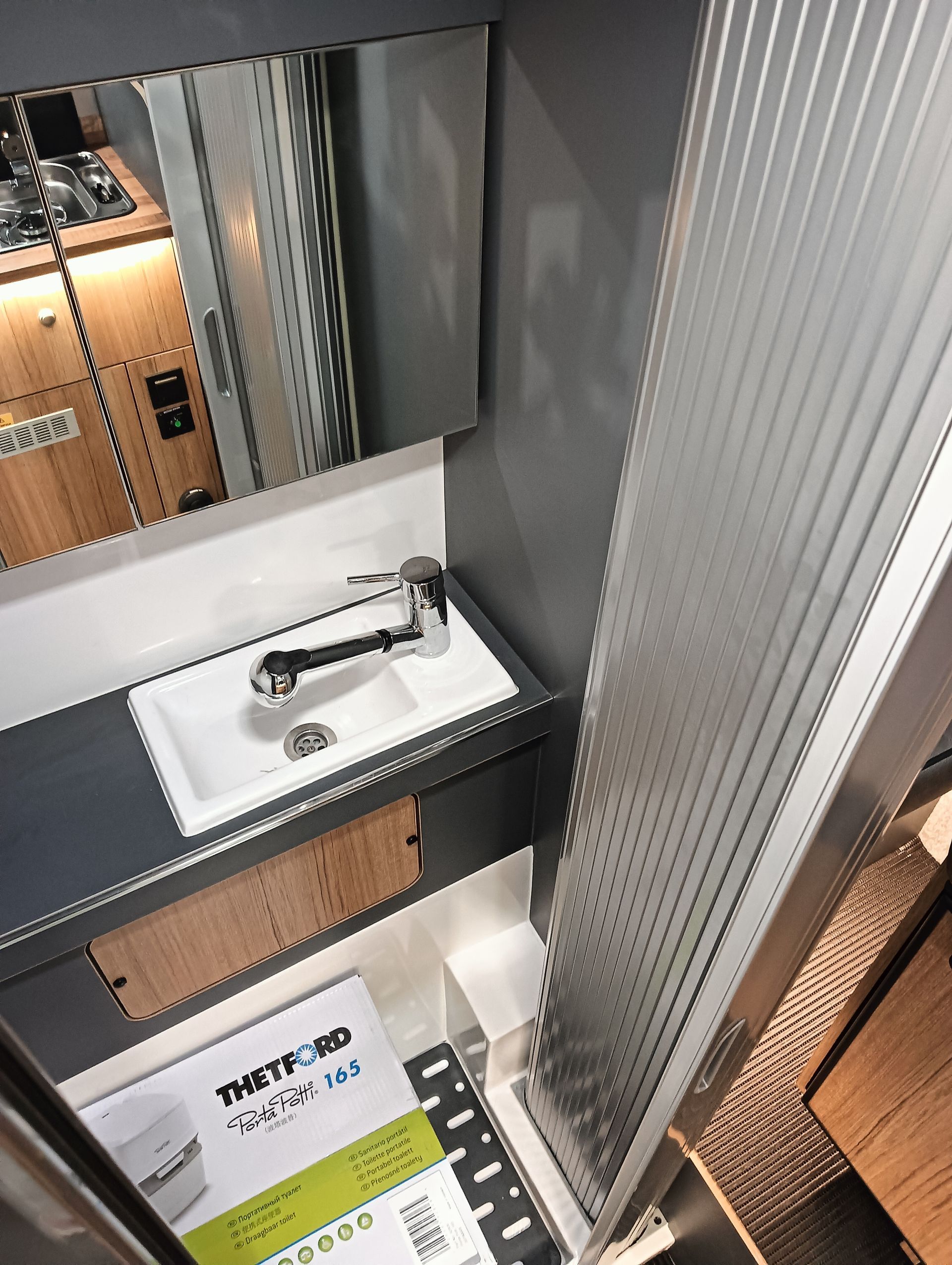 Piccolo bagno per camper con lavandino, specchio e tenda da doccia.