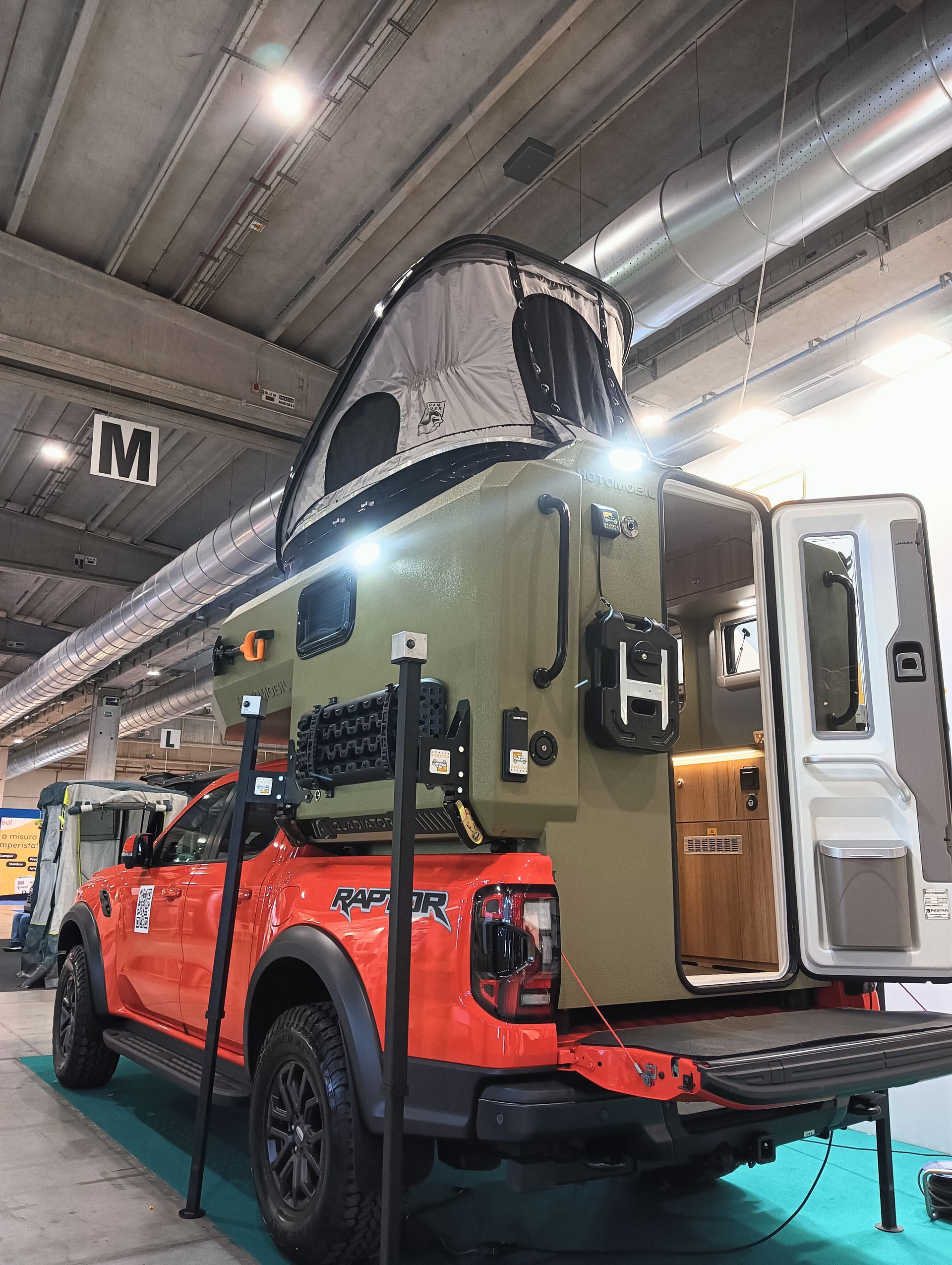 Camion Ford arancione con tetto verde tipo camper. Portellone posteriore aperto, interno visibile.