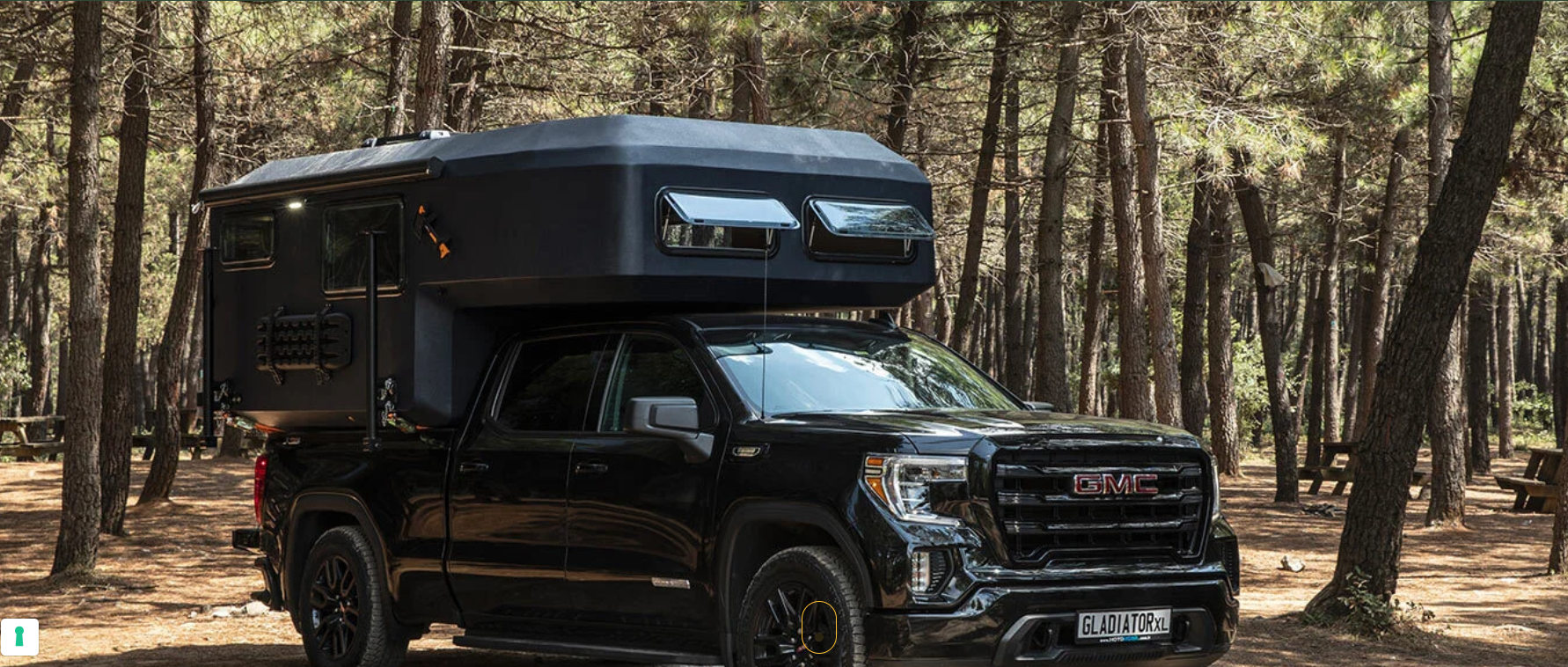Un camion nero con un camper sopra è parcheggiato nel bosco.