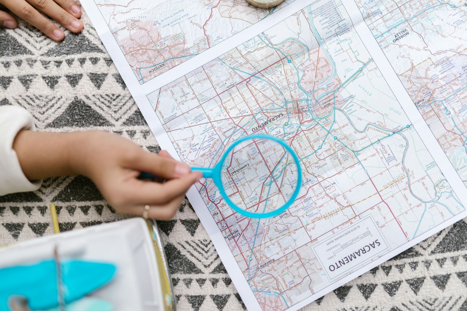 Persona che usa una lente d'ingrandimento per esaminare una mappa, con un vassoio e una superficie decorata.