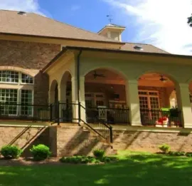 Large brick house with arched porch, green lawn, and clear blue sky