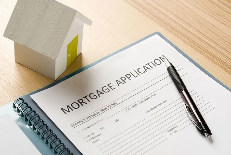 Mortgage application form beside a house model, with a pen on top