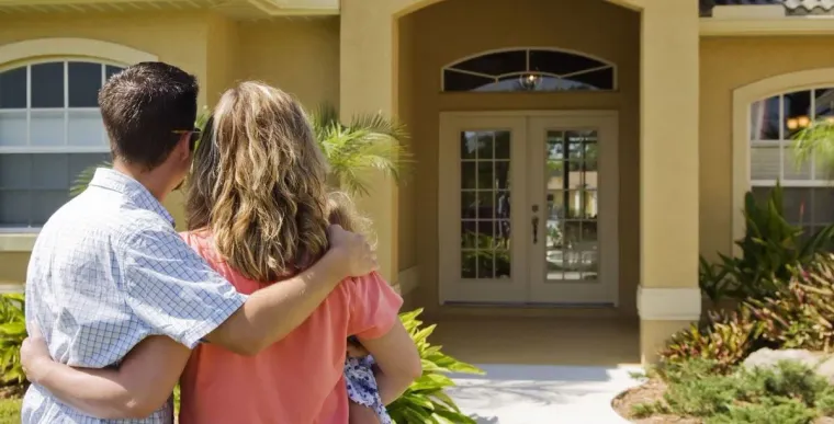 Two people embracing while facing a tan house with a front door and arched windows