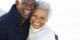 Two smiling people embracing outdoors against a bright white background