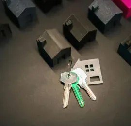 Set of keys on a black surface beside a small white device and miniature houses