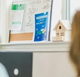 Office window shelf with notes, a blue brochure, and a small birdhouse model