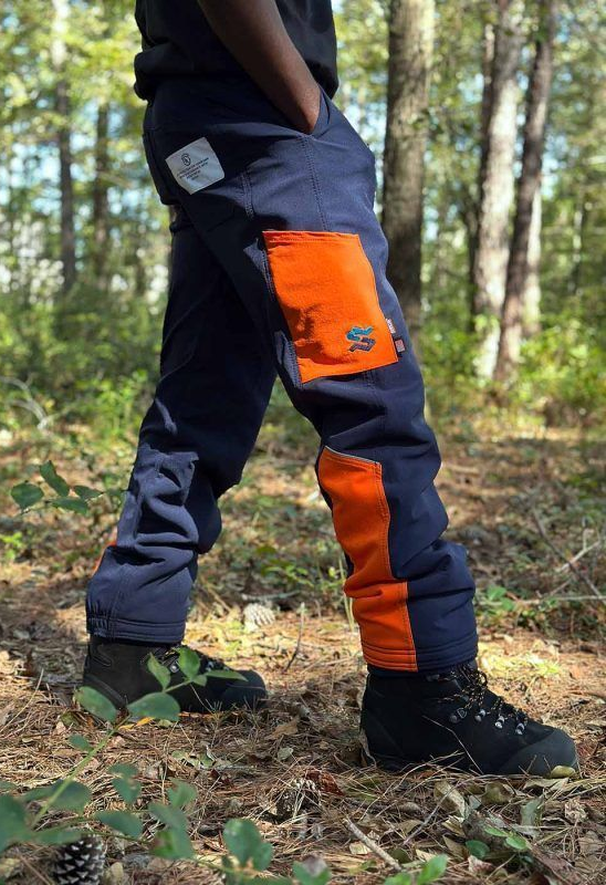 Person wearing navy and orange outdoor work pants standing in a wooded area